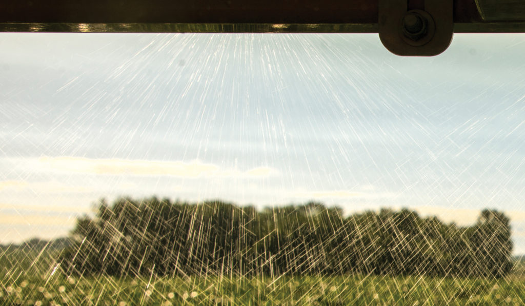Close-up image of agricultural spray equipment dispensing a herbicide over a growing crop.