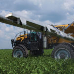 An AGCO RoGator with the AirMax 180 pneumatic spreader applies dry fertilizer to a corn field.